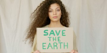 A young black woman with long curly hair holds a sign that says 'Save the Earth'.