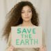 A young black woman with long curly hair holds a sign that says 'Save the Earth'.