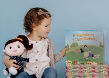 A small child holding a plush doll and holding up the Carry Kindness book