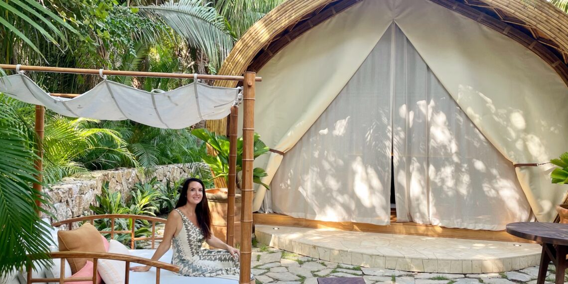 Woman sitting in a cabana in front of a luxury tent in the middle of a tropical forest.