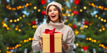 Happy smiling woman in a knitted hat and sweater holding a gift box.
